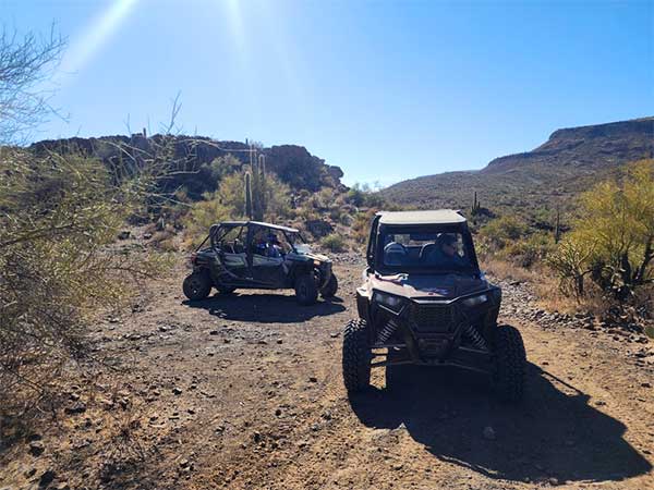 two UTV side-by-side vehicles parked on a deserted desert road during daytime