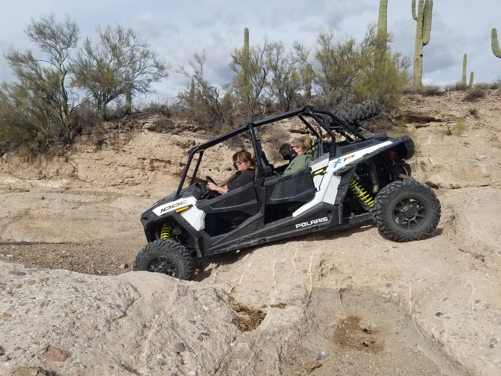 a white and black side-by-side UTV being driven over boulders in the desert
